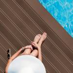 woman sitting on tobacco brown smart decking next to pool