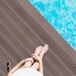 woman sitting on chocolate brown smart decking next to pool